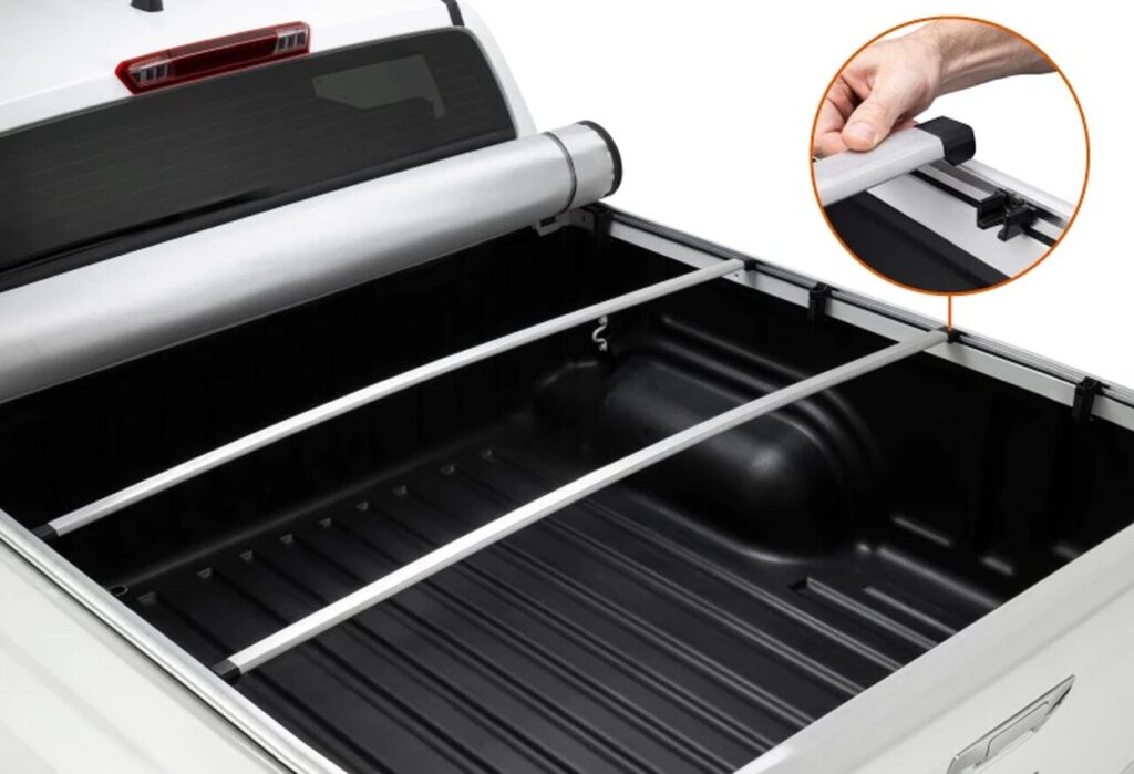 Imagem da caçamba de uma S10 branca equipada com a melhor capota da S10, modelo retrátil, parcialmente aberta para mostrar a funcionalidade e proteção do sistema. Três barras horizontais reforçam a estrutura, enquanto o mecanismo de travamento é demonstrado em detalhe, evidenciando segurança e praticidade.
