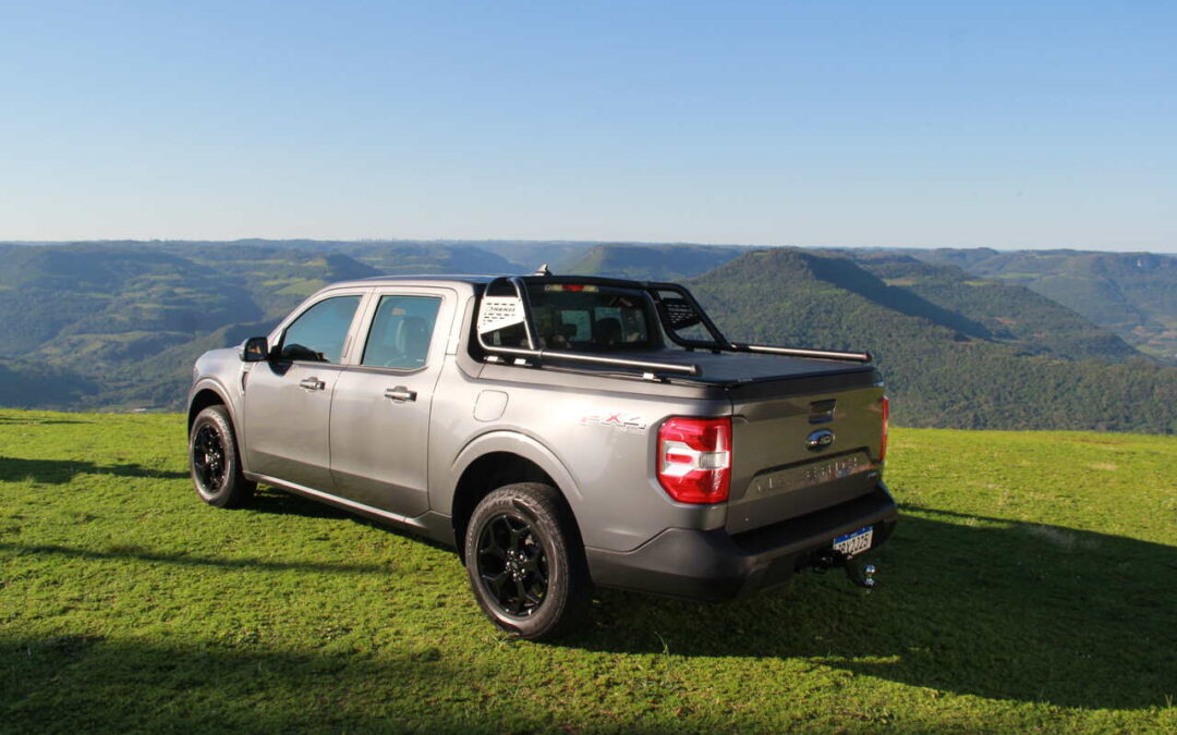 Picape cinza em colina gramada com vista montanhosa, destacando estilo off-road. Ideal para quem tem dúvidas sobre capotas marítimas e busca proteção e desempenho em aventuras ao ar livre.