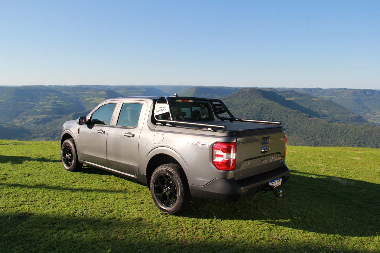 Picape cinza em colina gramada com vista montanhosa, destacando estilo off-road. Ideal para quem tem dúvidas sobre capotas marítimas e busca proteção e desempenho em aventuras ao ar livre.
